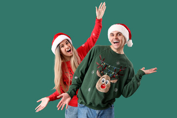 Canvas Print - Young couple in Santa hats and Christmas sweaters on green background