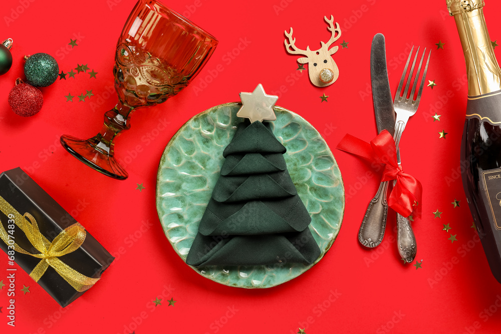 Beautiful table setting for Christmas dinner with champagne bottle and decorations on red background