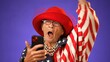 Closeup of funny crazy elderly old toothless woman answering smart phone call say wow as winner with success laughing and smiling. Wearing US American flag jacket solated on purple background