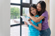 © kaew6566 - Happy asian LGBTQ lesbian woman looking tablet standing together beside window at living room. Lover young couple girl use tablet purchase shopping online hugging together aside window home.Technology