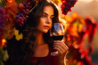 A charming woman stands with a glass of red wine in hand, surrounded by bunches of grapes bathed in the warm rays of the sun.