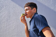 Young man eating avocado toast outdoors by gray textured wall 