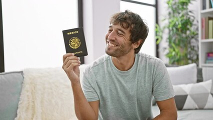 Sticker - Joyful young hispanic man confidently smiling, holding his mexican passport, sitting casually on the living room sofa at home, excited to plan his vacation trip.