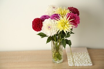 Canvas Print - Bouquet of beautiful Dahlia flowers in vase and notebook on wooden table near white wall