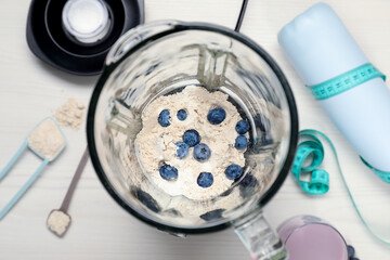 Wall Mural - Making shake. Blueberries and powder in blender on white table, top view