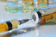 Filling syringe with orange medication from glass vial on white table, closeup