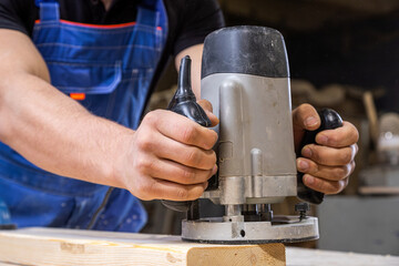 Wall Mural - Young man by profession carpenter builder equals a wooden milling machine on a wooden table in the workshop