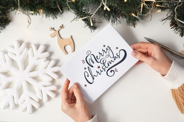 Mature woman with greeting card for Christmas celebration on white table, top view