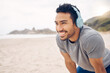 Break, beach and man workout to relax with a smile after cardio exercise. Fitness, jog and healthy athlete or male person rest in natural ocean with headphones for music and physical wellness