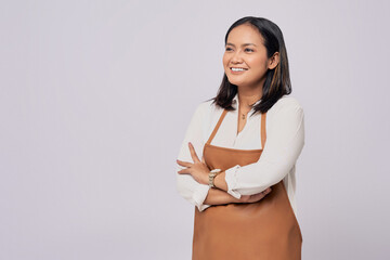 Wall Mural - Optimistic young Asian woman barista employee in brown apron working in coffee shop, standing with crossed arms, looking aside with smile isolated on white background. Small business startup