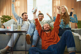 Fototapeta  - Bottom view of cheerful group of friends sitting on sofa in living room and watching basketball match and favorite team win victory,