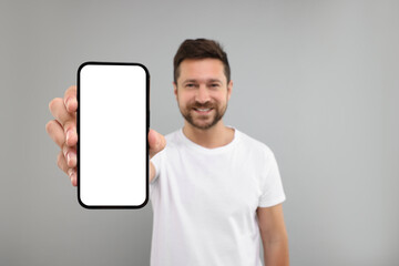 Wall Mural - Handsome man showing smartphone in hand on light grey background, selective focus. Mockup for design