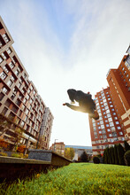 Free-runner Jumping In Air, Make Back Flip, Practice Parkour In Public Park Among High-rise Buildings Over Sunrise.