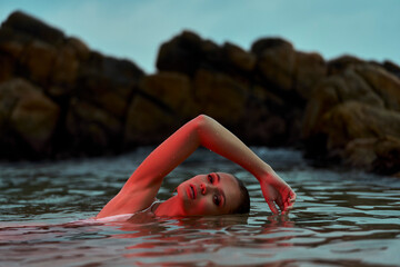 Woman enjoys serene swim in lagoon at dusk, nature's swimming pool, tranquil moment captured, wellness in natural habitat.