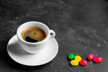 Espresso coffee in a white cup on a dark background with colored candies. There is free space for text