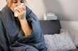 © TatjanaMeininger - Sick woman sitting on sofa with blanket and sneezing in a tissue