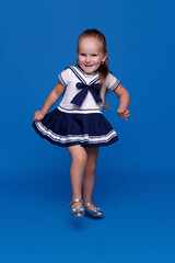 Wall Mural - Full length image of a cute little girl in dress, posing in studio, isolated blue background.