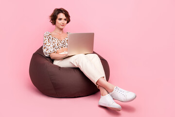 Poster - Full size photo of intelligent girl dressed print stylish blouse sit on pouf look at laptop write post isolated on pink color background