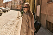 © LIGHTFIELD STUDIOS - young blonde woman in stylish trench coat and sunglasses walking on street in sunny day, urban chic
