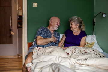 Wall Mural - Elderly couple sitting in bed and looking at each other with love
