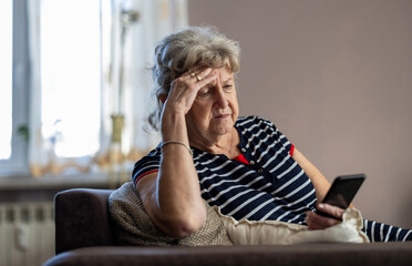 Wall Mural - Elderly woman sitting on couch and using mobile phone at home
