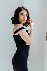 Wall Mural - Portrait of a young beautiful girl in a black dress on a white background