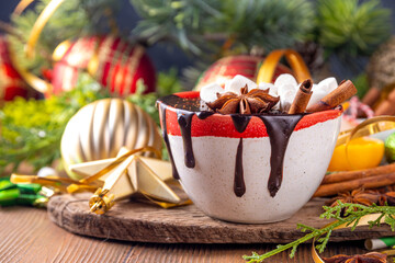 Wall Mural - Winter aromatic hot chocolate cup with Christmas background. Mug of dark hot cocoa drink with cinnamon, anise, spices and marshmallow, on cozy Christmas and New Year holiday decorated background 