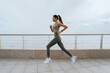 © Iona - beautiful slender brunette, sportswear and a fitness bracelet runs along the embankment, does sports, develops  endurance. Asian young woman doing an outdoor workout. Active people, healthy lifestyle