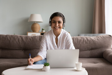 Canvas Print - Portrait of happy young student busy in self-education use laptop and internet resources gaining new knowledge improve skills. Cheerful Indian woman in headphones looks at camera e-learning at home