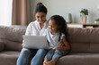 © fizkes - Cute little girl using laptop sit on sofa with loving mom, parent teach child to use modern device for education or fun, spend leisure at home. Family e-shopping via website, on-line purchases concept