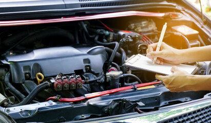 Hands woman auto mechanic hold checklist for checking car breaks on car engine background for maintenance or repair service concept.