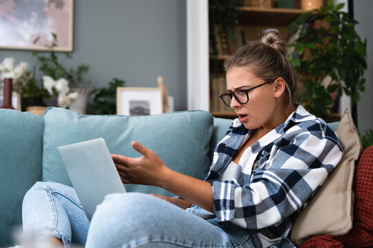 Confused young woman looking on laptop at home feeling bewildered by no connection, reading online news in internet, annoyed teen girl angry with stuck computer problem, scam spam email, system error
