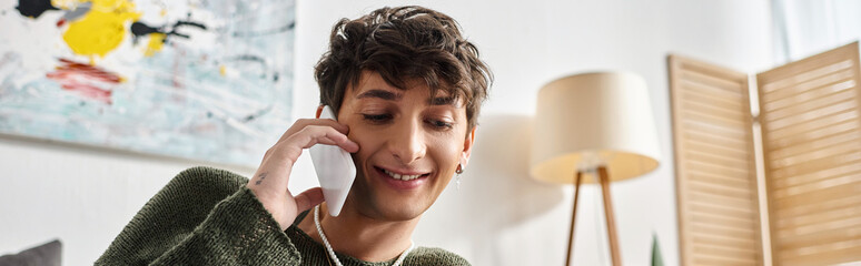 happy and curly transgender person in casual attire talking on smartphone in bedroom, banner