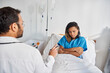 © LIGHTFIELD STUDIOS - attractive ill african american woman lying in hospital bed listening her young indian doctor