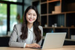 © Bojan - Asian business woman using laptop and smiling at camera in a office.