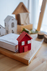 Wooden red house to decorate the house for the Christmas holidays. Wooden toy for the Christmas tree. A candle in a jar is burning in the background. Juniper branches. Handmade product.