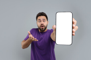 Canvas Print - Surprised man showing smartphone in hand on light grey background, selective focus. Mockup for design