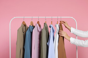 Wall Mural - Woman taking stylish jacket from clothes rack against pink background, closeup