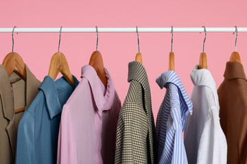 Wall Mural - Rack with stylish clothes on wooden hangers against pink background, closeup