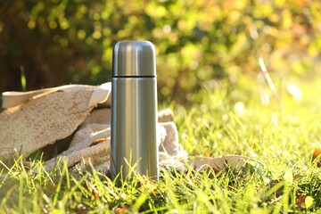 Canvas Print - Metal thermos and bag with blanket on green grass outdoors, space for text