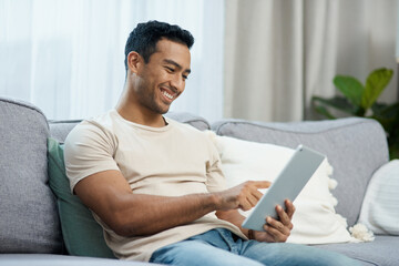 Wall Mural - Tablet, smile and relax with a man on a sofa in the living room of his home for social media browsing. Technology, app or gaming search with a happy young person in his apartment on the weekend