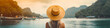 Rear view of young woman in a hat and swimsuit sitting on a boat in the tropical island bay, colorful bokeh, panoramic header, generative ai
