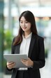© yj - Busy young Korea business woman executive holding pad computer at work. East Asian female professional employee using digital tablet fintech device standing in office checking data. generative AI