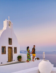 Wall Mural - Men and women visit the whitewashed Greek village of Oia Santorini, a couple watching the sunrise in Santorini during vacation
