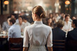 Back view of young waitress in restaurant full of people
