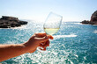 A man's hand holds a glass of champagne against the backdrop of the sea and mountains. Vacation concept