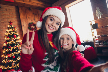 Sticker - Photo of positive cute little siblings dressed ugly print christmas jumpers cuddling showing v-sing recording video vlog indoors house room