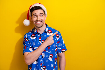 Sticker - Photo of young guy brunet hair wear santa claus hat indicating finger mockup happy new year event isolated on yellow color background