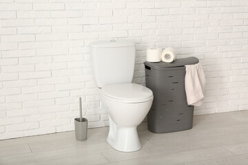 Wall Mural - Rolls of paper rolls on toilet bowl and laundry basket near light brick wall