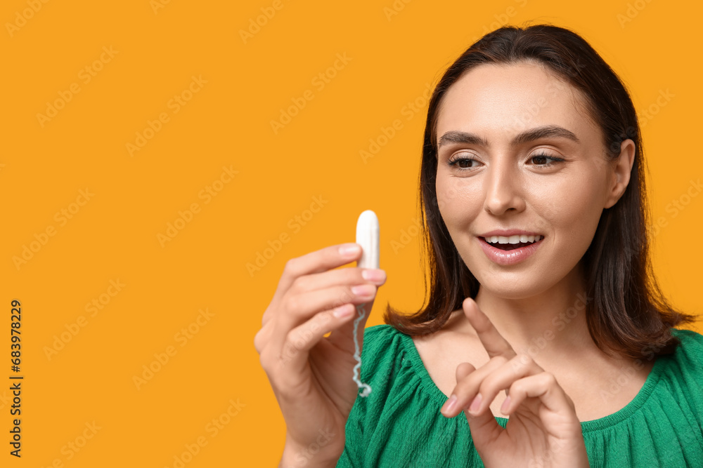 Beautiful young woman with tampon on yellow background